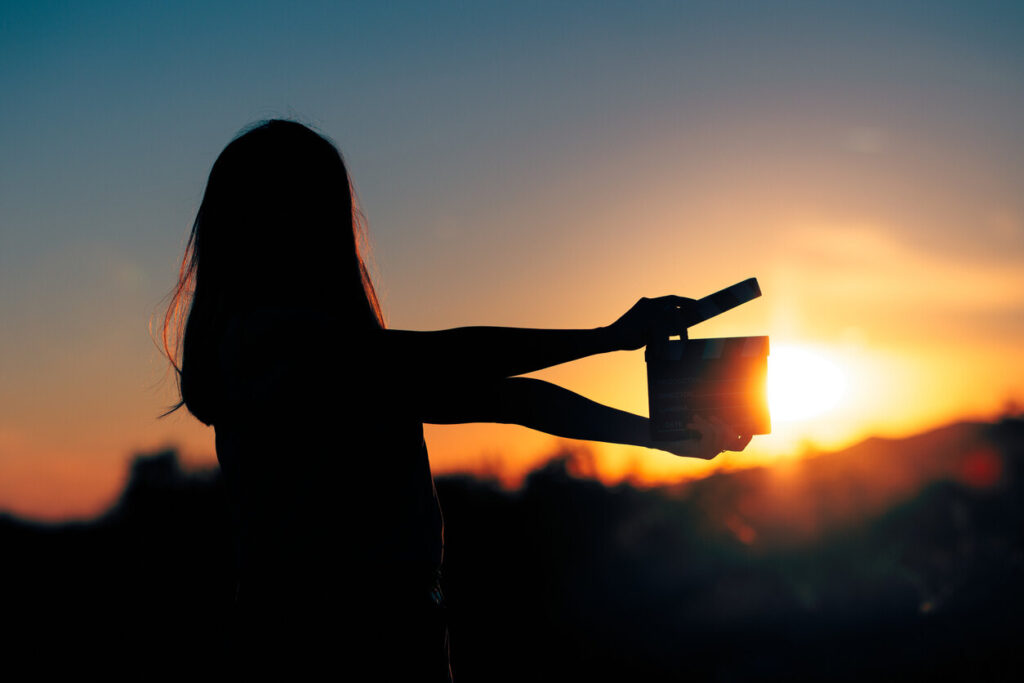 Silhouette of an entertainment industry worker holding a film clapperboard at sunset, representing California workers in movie industry